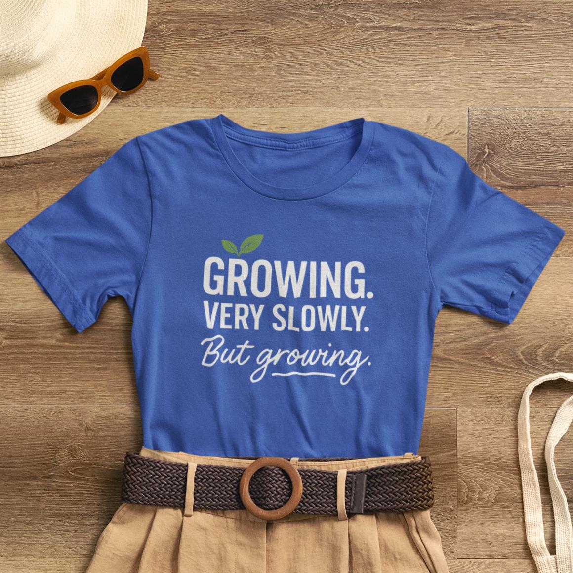 Light-colored T-shirt with "Growing Very Slowly But Growing" text, emphasizing gentle growth and emotional healing, by Printify.