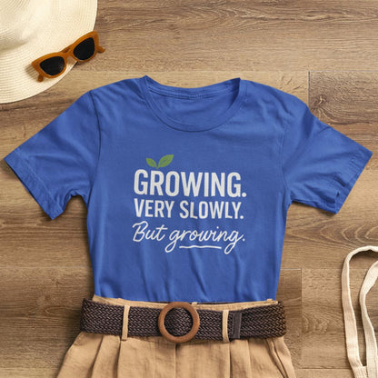 Light-colored T-shirt with "Growing Very Slowly But Growing" text, emphasizing gentle growth and emotional healing, by Printify.