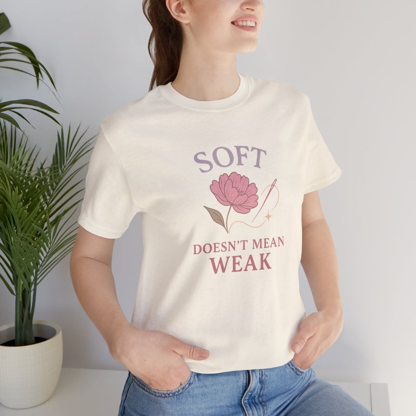 Feminist floral empowerment T-shirt by Printify with bold "Soft Doesn’t Mean Weak" slogan in vibrant colors.