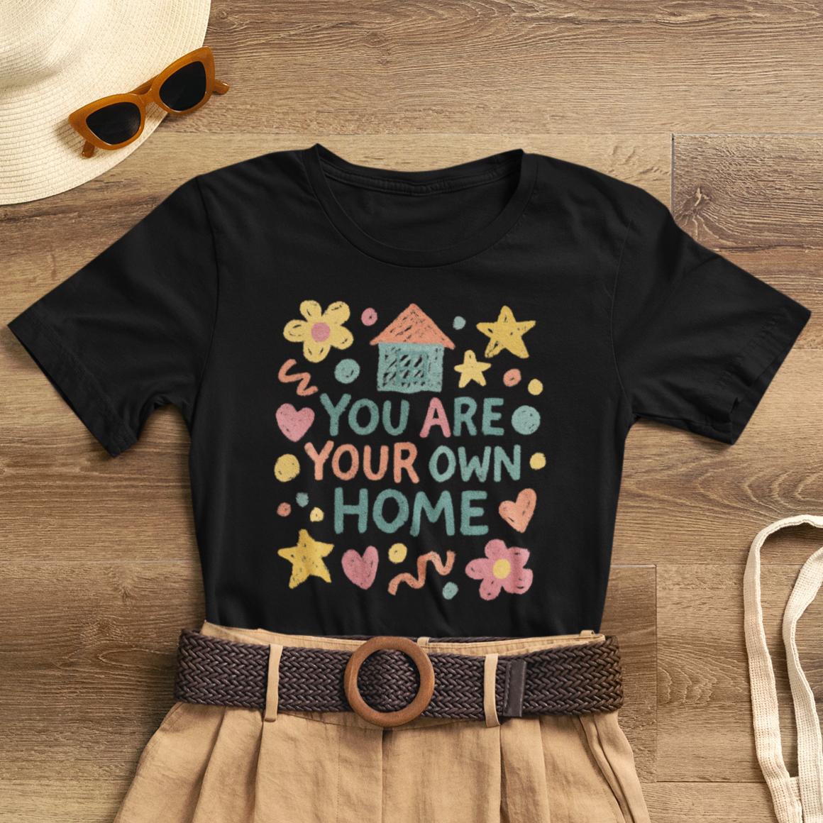 Pastel doodle tee featuring "You Are Your Own Home" quote, soft fabric, and naive art aesthetic by Printify.